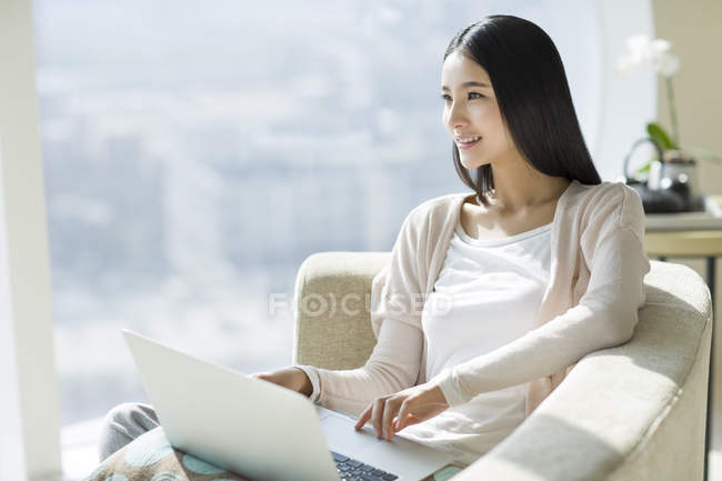 Donna cinese che utilizza il computer portatile sul divano in casa interna — Foto stock