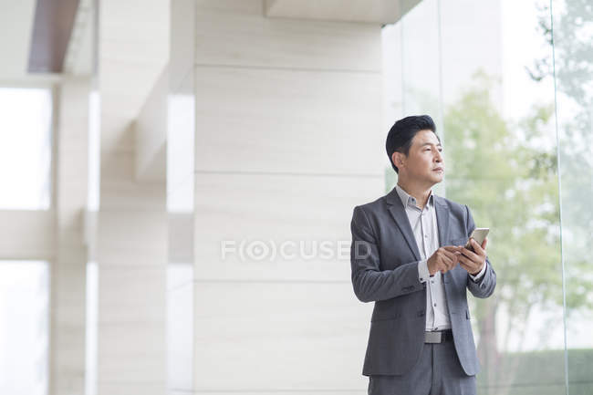 Азіатський бізнесмен, що стоїть перед скляні двері з смартфон — стокове фото