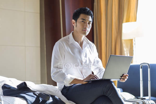 Uomo d'affari cinese che utilizza laptop sul letto in camera d'albergo — Foto stock