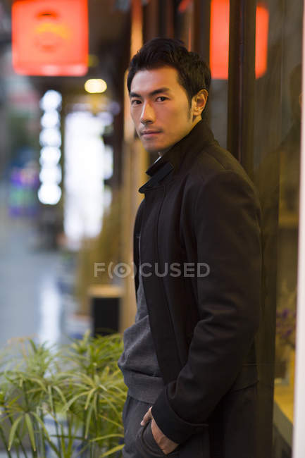 Азиатский мужчина склоняется к витрине магазина на городской улице — стоковое фото
