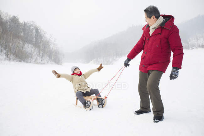 Grand-père chinois tirant petit-fils sur traîneau — Photo de stock
