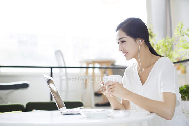 Chinese woman listening to music in coffee shop — Stock Photo