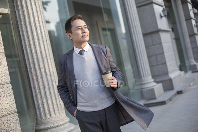 Uomo d'affari cinese in possesso di caffè e guardando la vista in città — Foto stock