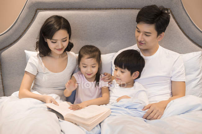 Pais chineses e crianças lendo livro na cama — Fotografia de Stock