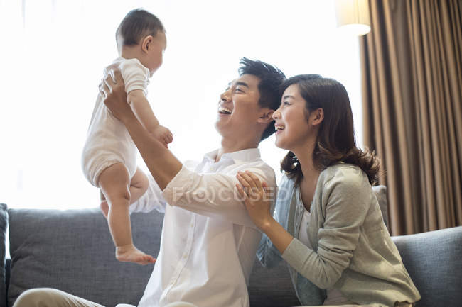 Genitori cinesi che tengono il bambino e sorridono sul divano — Foto stock