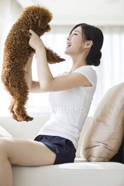 Jeune femme chinoise jouer avec animal caniche sur canapé — Photo de stock