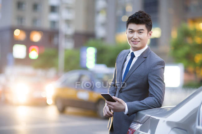 Empresário chinês de pé ao lado do carro com smartphone — Fotografia de Stock