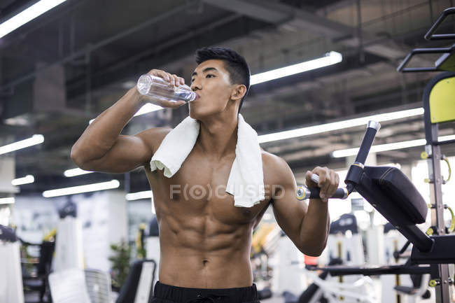 Chinese man resting and drinking water at gym — Stock Photo