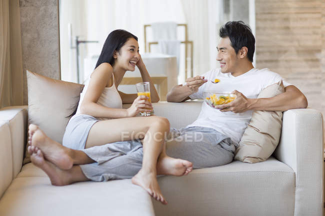Casal chinês tomando café da manhã no sofá — Fotografia de Stock