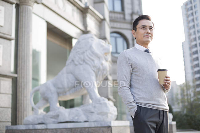 Китайский бизнесмен держит кофе и смотрит на город — стоковое фото