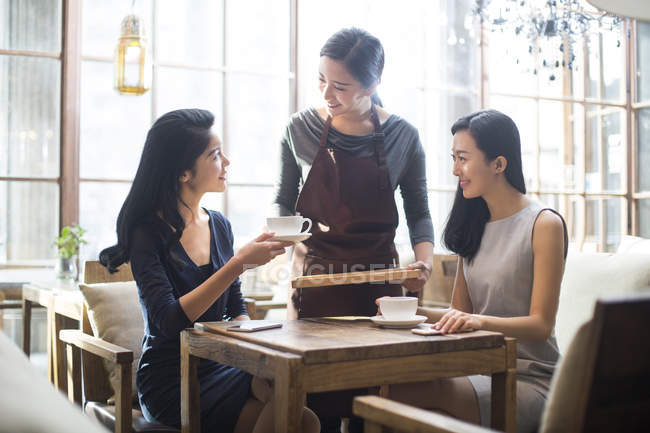 Camarera china sirviendo café a amigas en la cafetería - foto de stock
