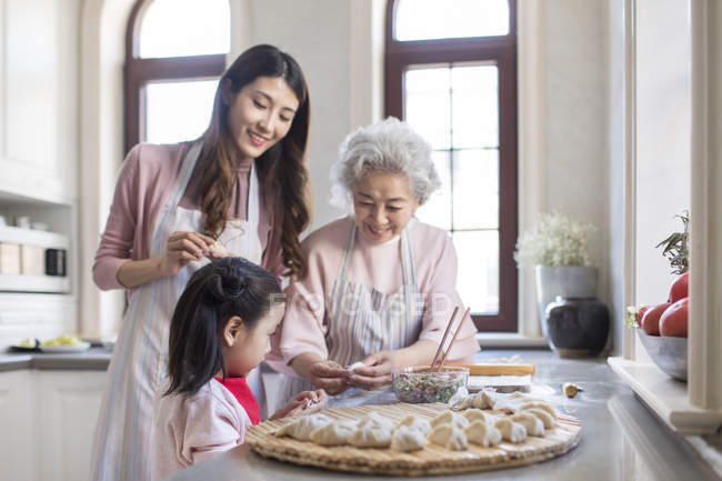 Familia china haciendo albóndigas en la cocina - foto de stock