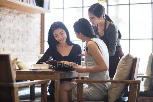 Chinese female friends ordering with waitress in cafe — Stock Photo