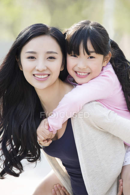 Asian mother riding daughter piggyback — Stock Photo