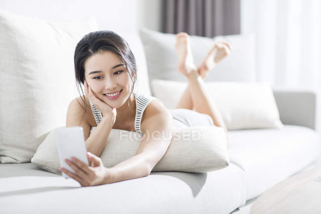 Mulher asiática usando smartphone no sofá em casa interior — Fotografia de Stock