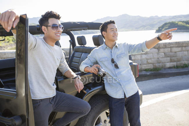 Uomini cinesi appoggiati su auto in periferia e che puntano — Foto stock