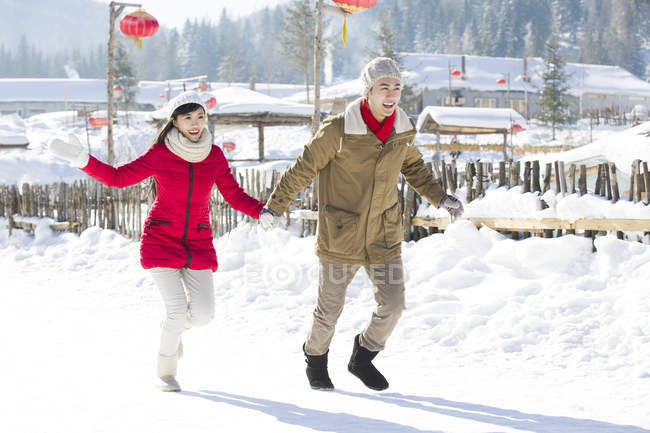Chinese couple holding hands and running in snow — Stock Photo