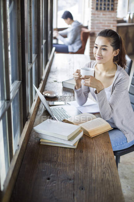 Mulher chinesa estudando com xícara de café no café — Fotografia de Stock