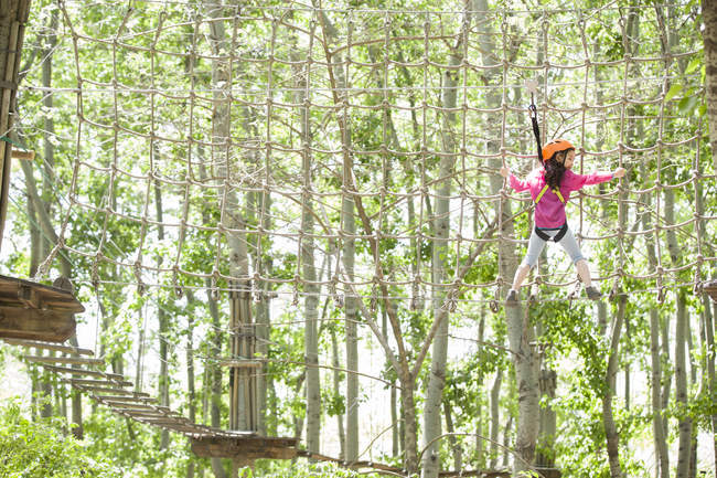 Chica china trepando en la red en el parque de aventura árbol superior - foto de stock
