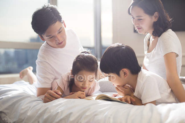 Chinese parents and children reading book in bed — Stock Photo