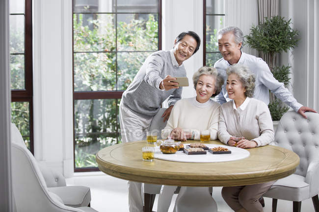 Senior Chinese friends taking selfie with smartphone while tea party — Stock Photo