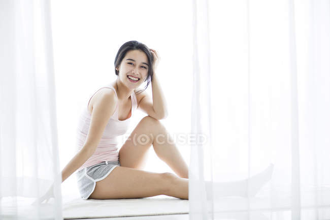 Азиатка, сидящая на подоконнике утром — стоковое фото