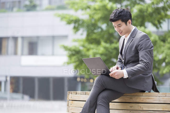Uomo d'affari cinese che lavora con laptop su panchina — Foto stock