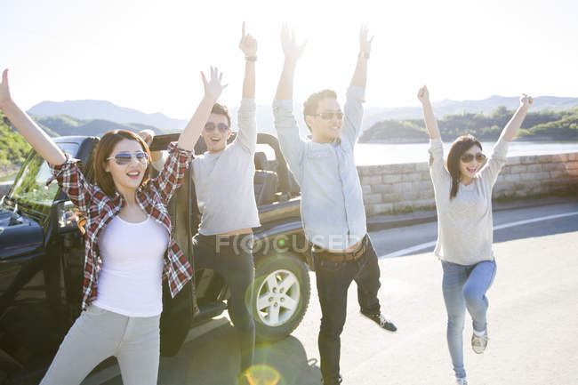 Chinese friends posing with arms raised in front of car — Stock Photo
