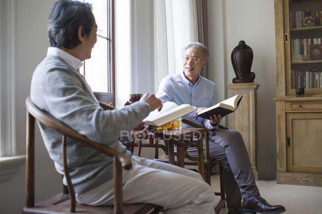 Senior Chinese men discussing while reading books in living room — Stock Photo