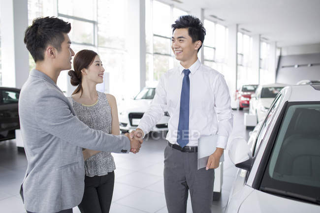 Chinese couple shaking hands with car dealer in showroom — Stock Photo
