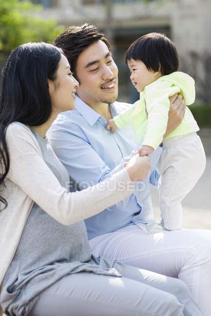 Asiática familia con bebé niña sentado en parque - foto de stock