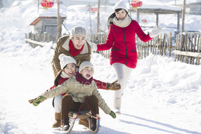 Família chinesa brincando com trenó na neve — Fotografia de Stock