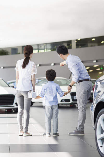 Chinese family in car dealership showroom pointing on cars — Stock Photo