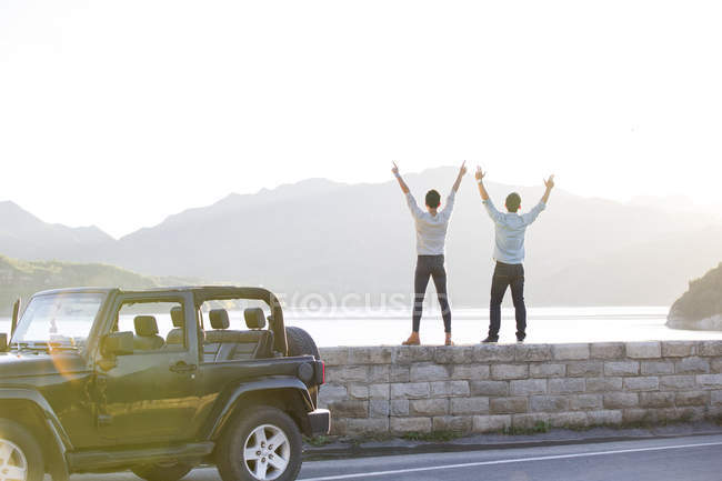 Чоловіки стоять на березі озера з піднятими руками — стокове фото