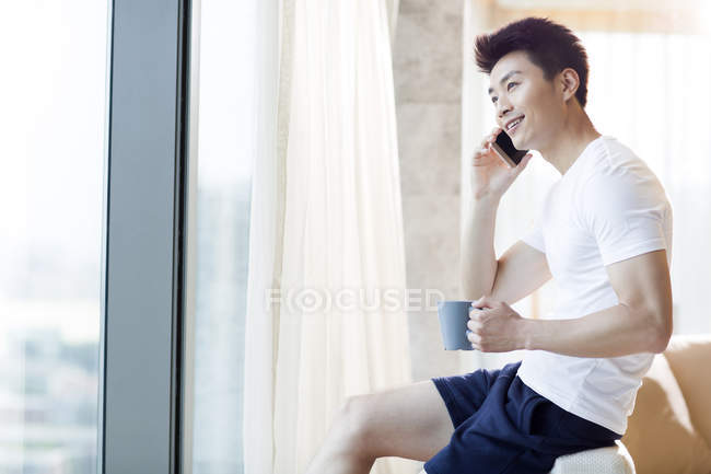 Homem chinês com café falando no telefone em casa — Fotografia de Stock