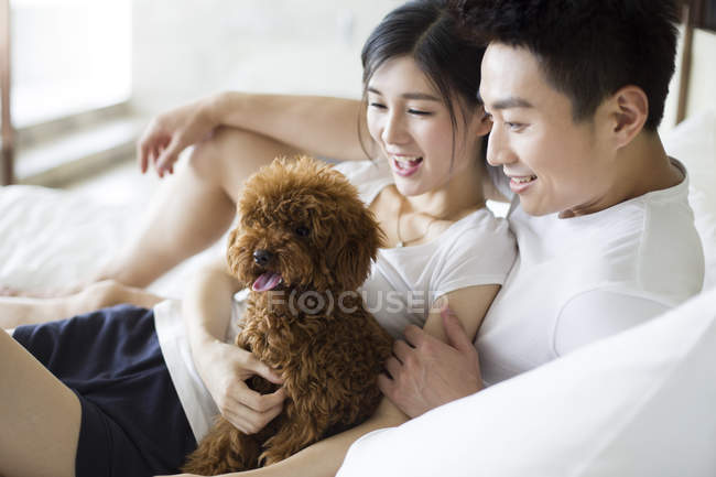 Jeune couple chinois jouer avec animal caniche à la maison — Photo de stock