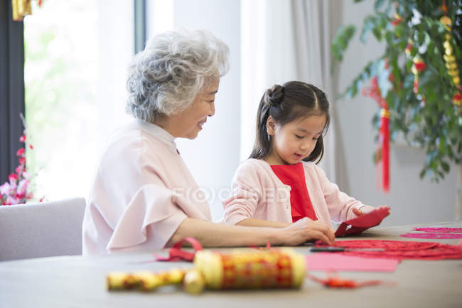 Nieta y abuela haciendo chino Año Nuevo papel-corte - foto de stock