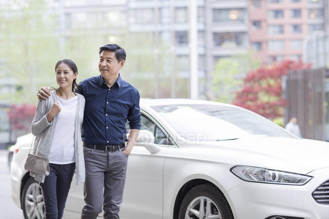 Mature chinese couple walking on street by car — Stock Photo