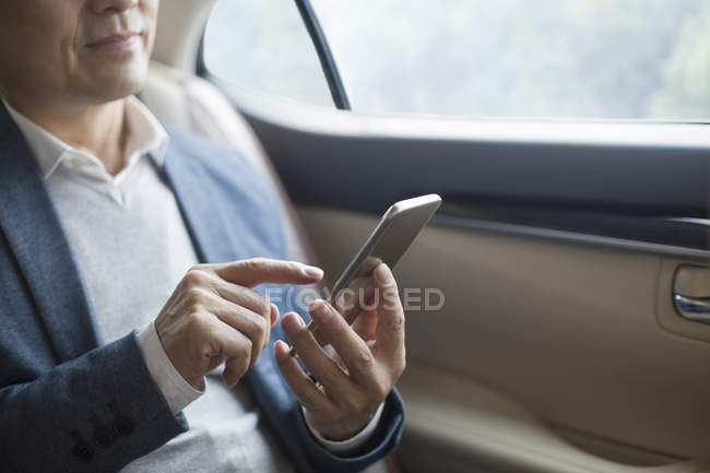 Asiatischer Geschäftsmann mit Smartphone auf Rücksitz im Auto — Stockfoto
