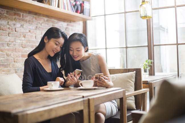 Amis chinoises utilisant des smartphones dans un café — Photo de stock