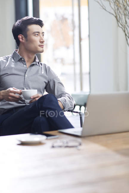Asian man drinking coffee in office — Stock Photo