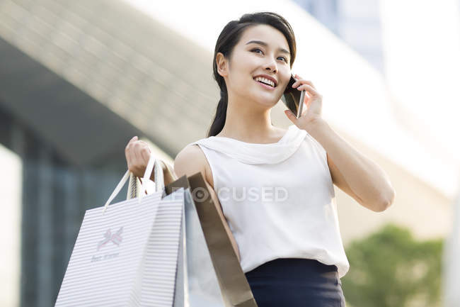 Asian woman talking on phone with shopping bags on street — Stock Photo