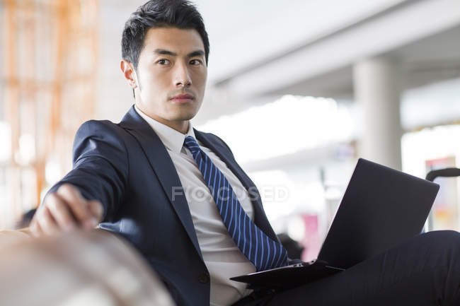 Chinese businessman sitting with laptop in airport waiting room — Stock Photo
