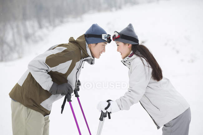 Chinese couple standing face to face with ski poles — Stock Photo