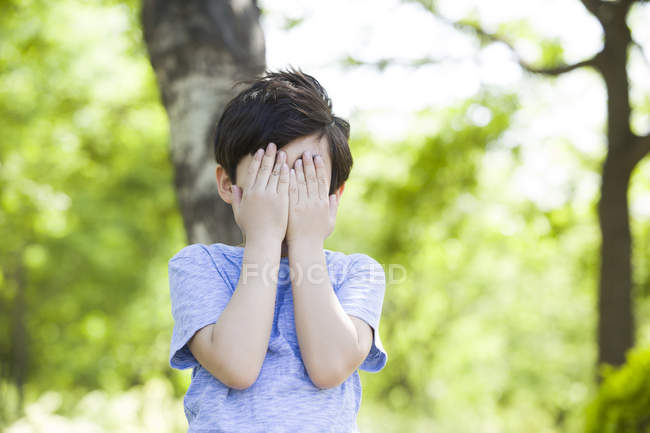 Preteen boy covering eyes in woods — Stock Photo