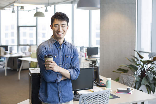 Portrait of young Chinese man with coffee in office — Stock Photo