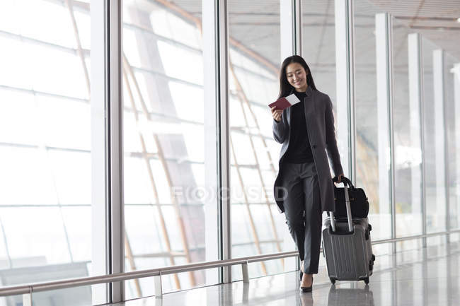 Asian woman pulling luggage in airport lobby — Stock Photo