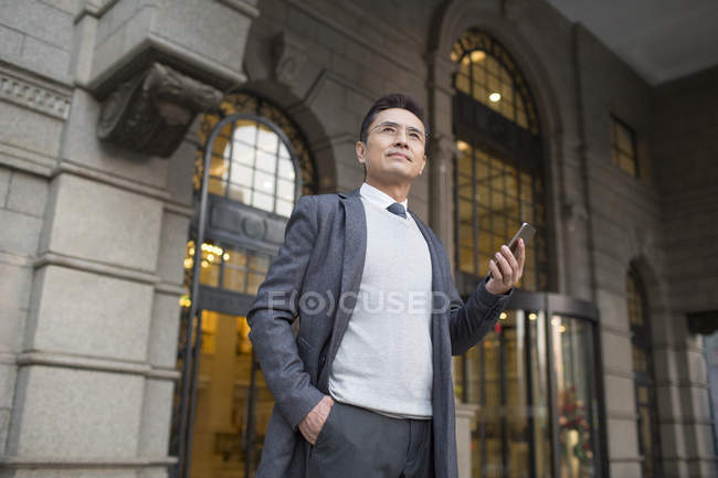 Chinese businessman holding smartphone in city — Stock Photo