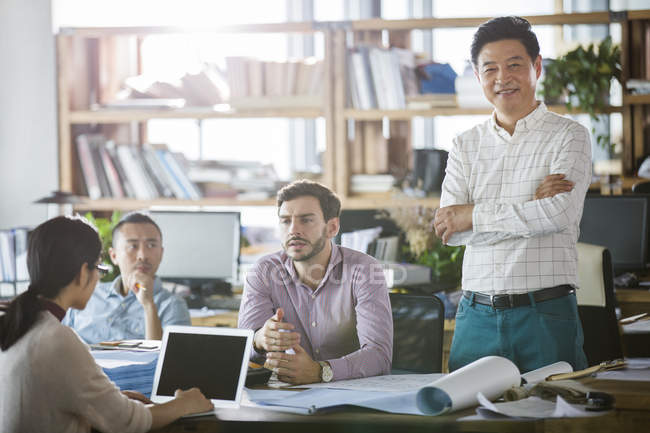 Architects discussing work in office while mature man smiling and looking in camera — Stock Photo