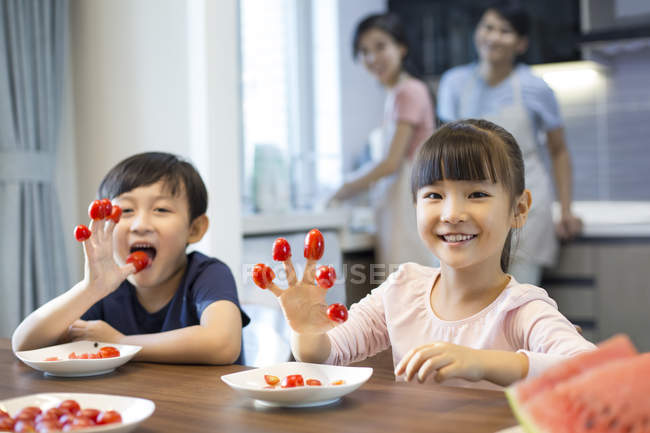 Frères et sœurs chinois jouant avec des tomates cerises avec leurs parents en arrière-plan — Photo de stock
